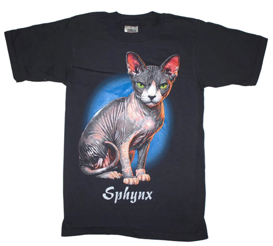 A black short-sleeve graphic t-shirt featuring a detailed illustration of a hairless Sphynx cat with green eyes and pink ears, set against a blue circular background with the word 'Sphynx' printed below in white gothic font.
